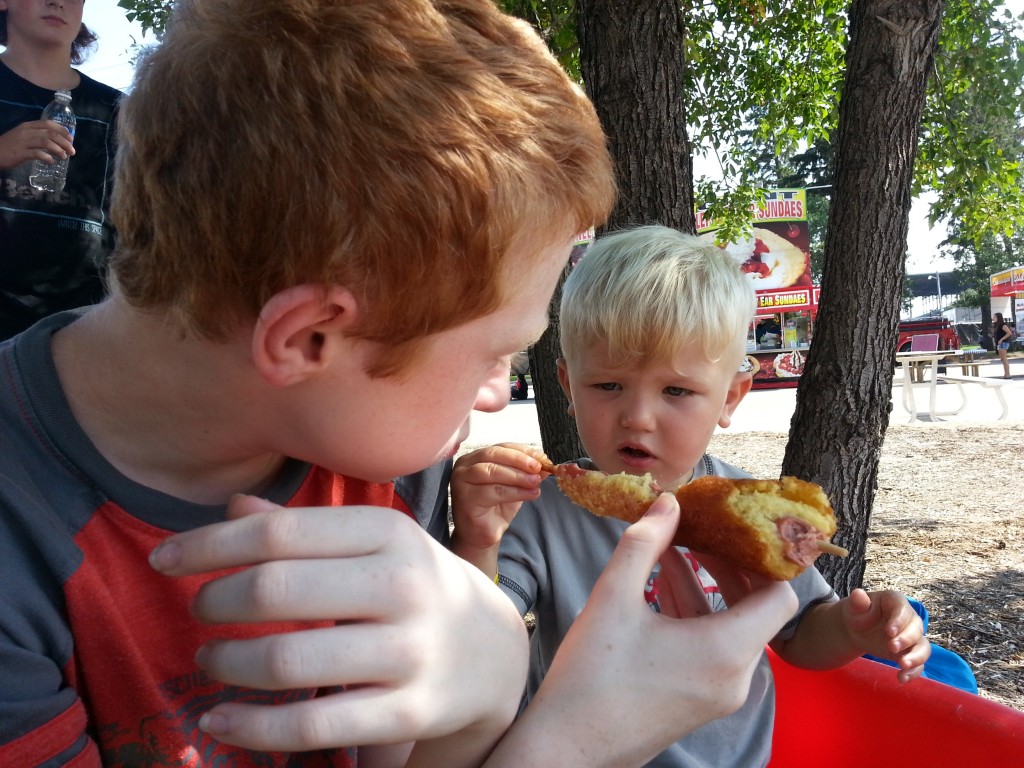 Sharing a corn dog with his cousin at the Ex.