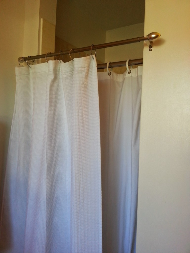 AFTER: Shower threshold makeover hack using two shower curtains and curtain rods - one inside to keep the water in the shower and one outside to hide the funky shower threshold.